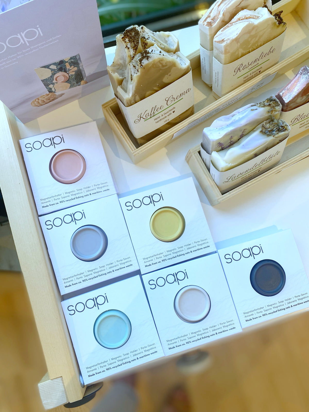 6 bunte Seifenhhalter im Display auf einem reagl neben handgesiedeten Seifen