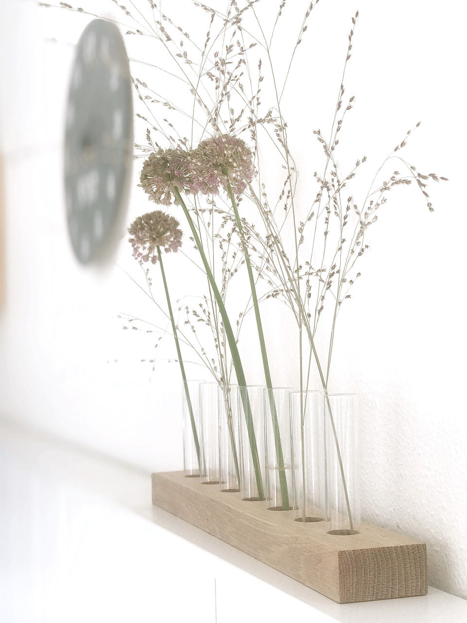 Blumenwiese mit sieben Glasröhrchen von Stadtrandstil. Seitenaufsicht auf weißem Bord, gefüllt mit getrockneten Blumen, im Hintergrund eine runde Wanduhr