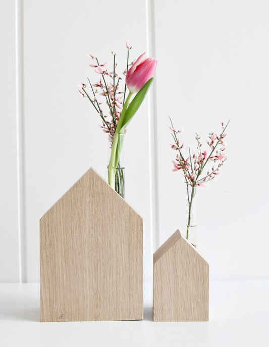 Zwei Blumenhäuser von Stadtrandstil, nebeneinander vor weißem Hintergrund, dekoriert mit rosafarbener Tulpe und Ginster