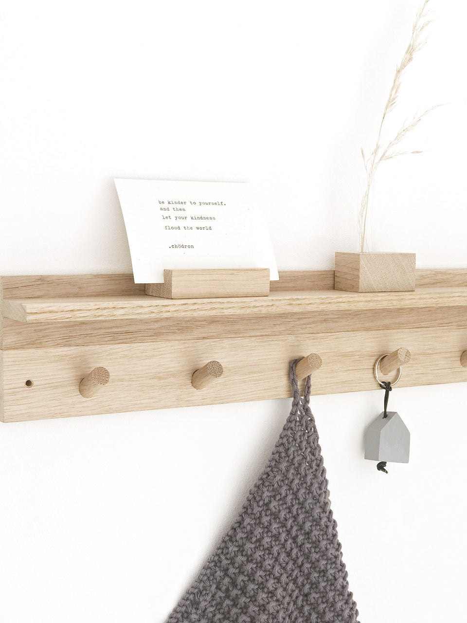 Schrägansicht einer Hakenleiste aus Eiche mit Ablagebord. Darauf steht ein kleiner Kartenhalter mit einer Karte und eine Minivase mit getrocknetem Gras. An den Haken hängz ein Schlüsselanhänger mit einem Minihasu und ein gestricktes dunkelgraues kleines Tuch