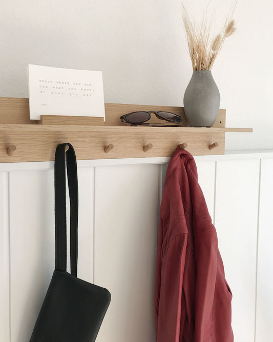Große Hakenleiste aus Eiche vmit einem Bord. Daruf stehen verschiedene Dekoelemente und an zwei Haken hängen eine rote Jacke und eine schwarze Handtasche