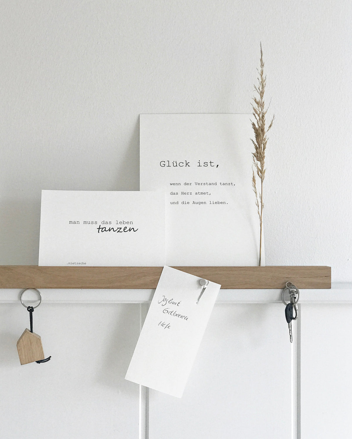 Wandleiste von Stadtrandstil handmade, natürlich und zeitlos dekoriert mit weißen Postkarten mit Text, einem getrocknetem Gras, einem Einkaufzettel. Fahrradschlüssel und einem Schlüsselanhänger in Hausform