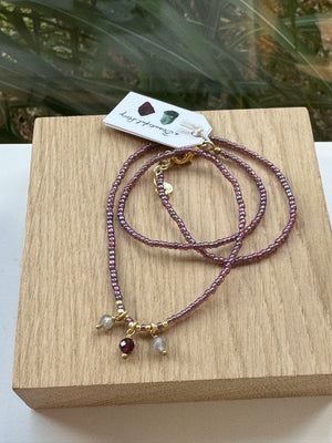 kette mit brombeerfarbenen Glasperlen und Rosenquarz auf Holzplatte