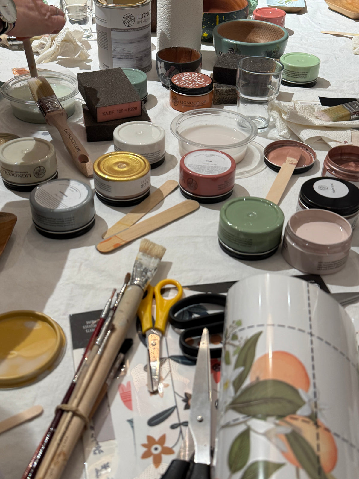 Arbeitstisch beim Workshop Holzschalen design mit Farbtöpfen, Rub ons und Werkszeugen