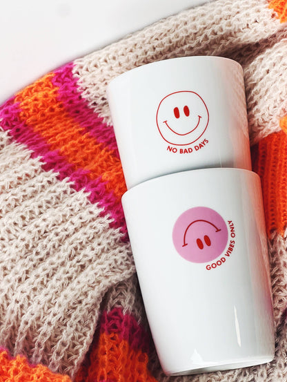 Zwei weiße Becher mit einem roten Smiley und dem Aufdruck "no bad days" und rosa Smiley und "good vifes only"