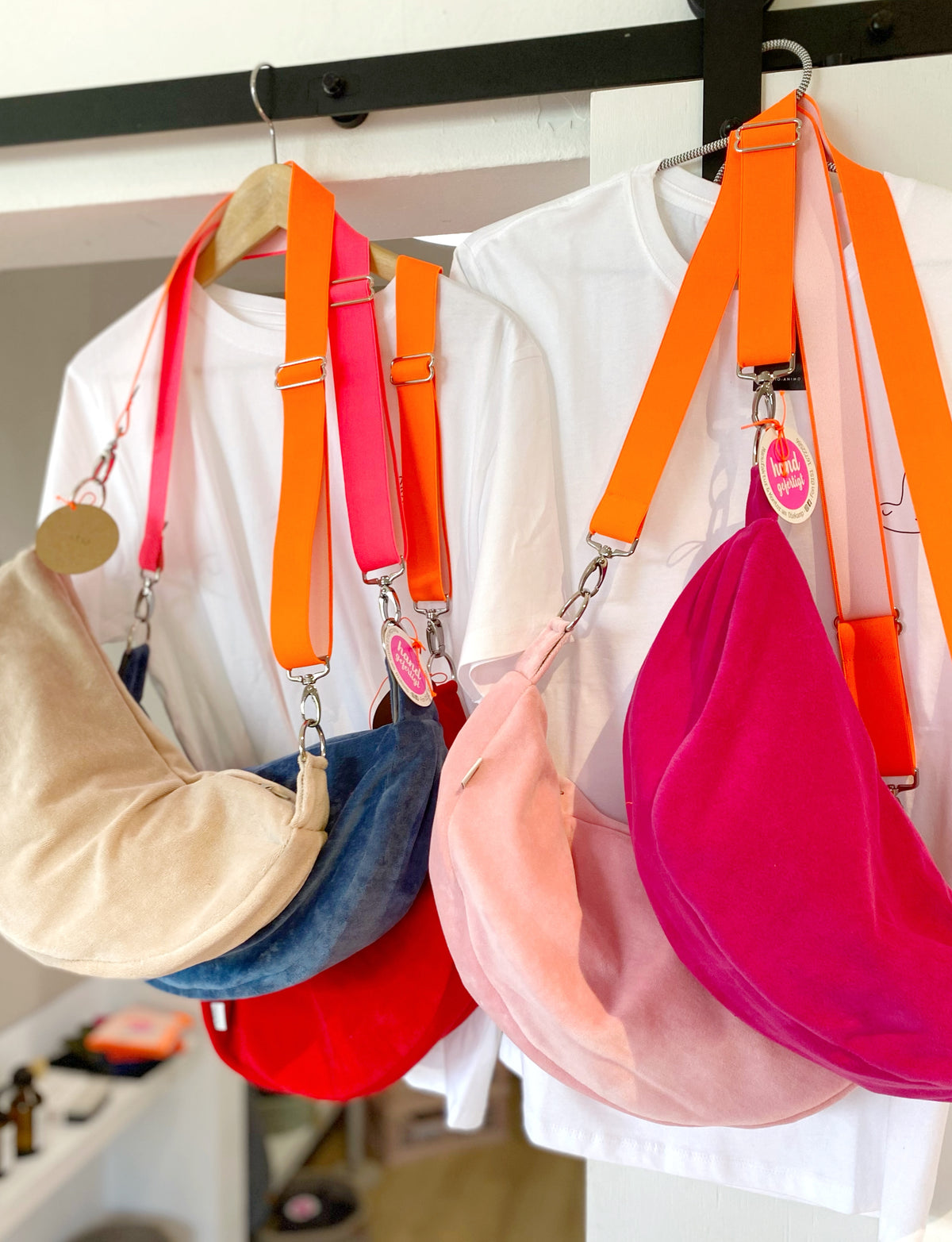5 Crossbody Bags in unterschiedlichen Farben mit Neon Gurten hängen vor weißen T-Shirts