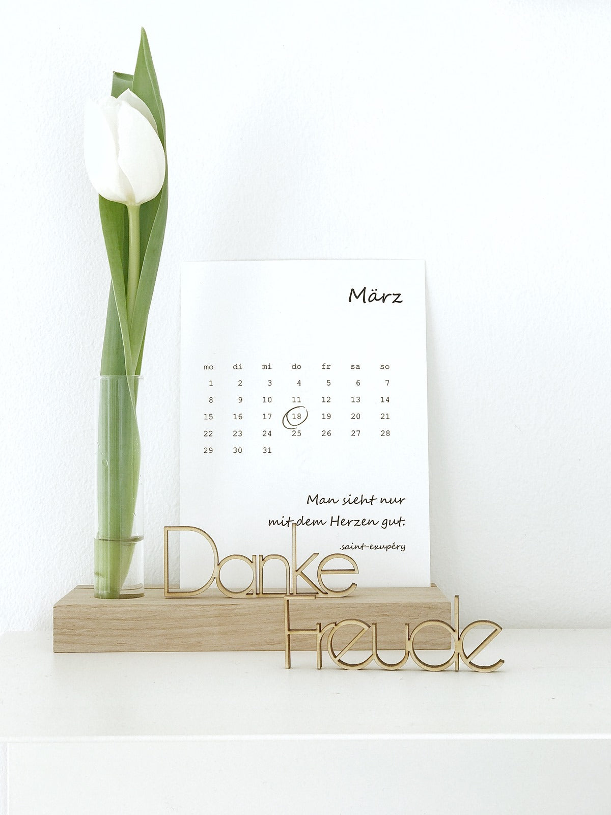 kleine Schriftzüge aus Holz "danke" und "freude" auf einem KAlenderhalter mit einem Reagenzglas und Tulpe