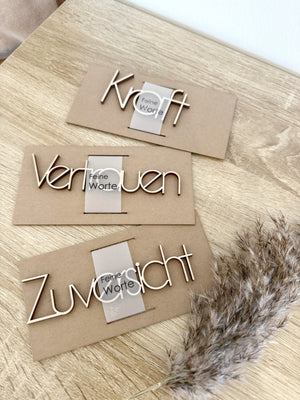 Schriftzüge aus Hole : "Kraft", "Vertrauen", "Zuversicht"auf Pappe neben Trockengras