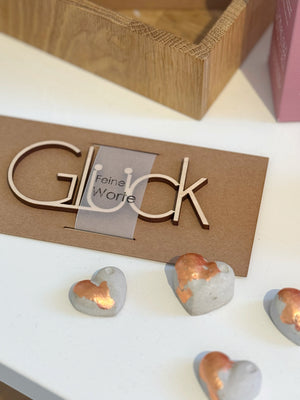 Schriftzug "Glück" aus Holz neben Betonherzen