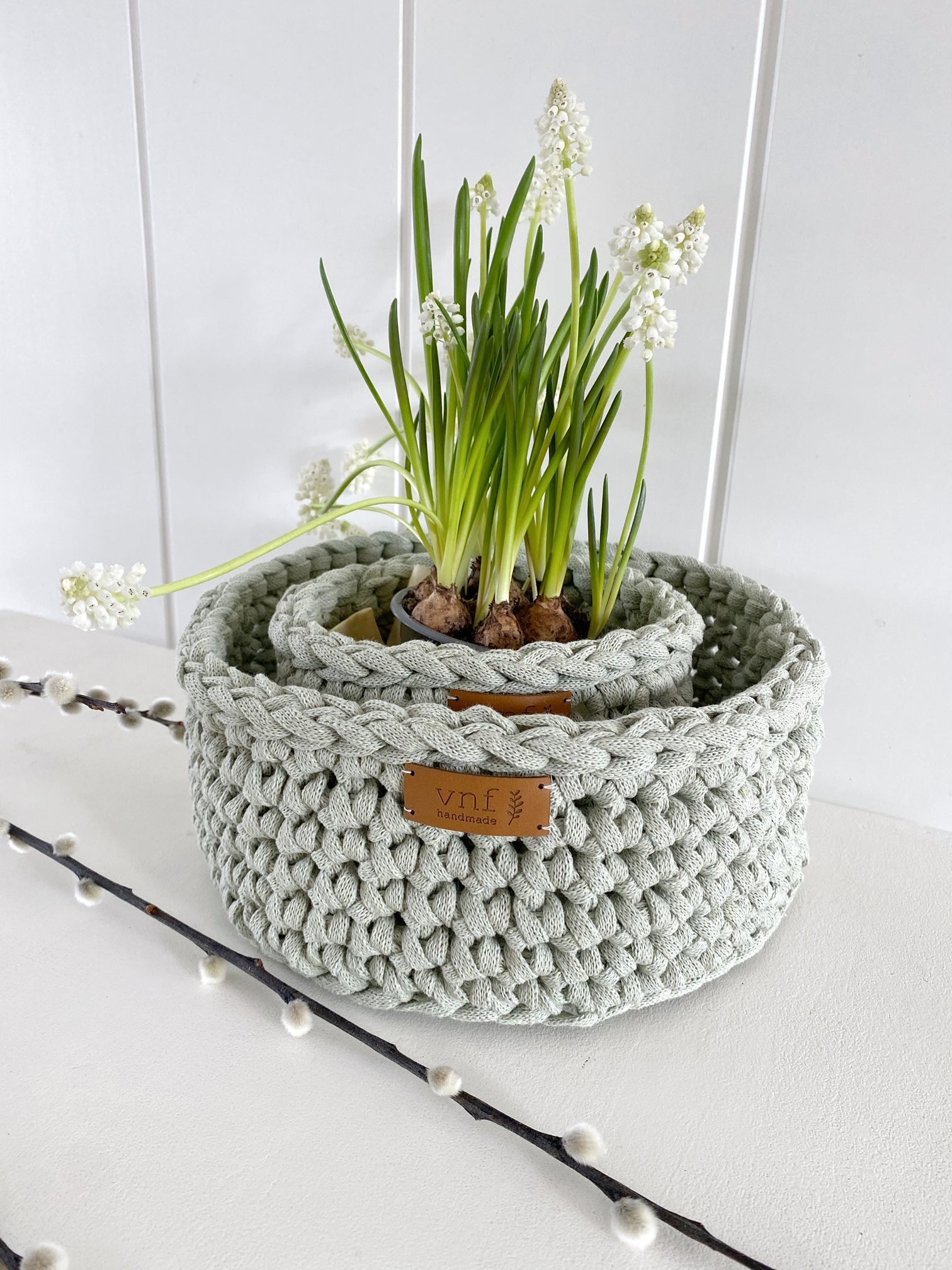 Zwei salbeifarbene ineinandergestellte Körbe verbreiten Frühlingsambiente. Im kleinerem steht ein Topf mit weißen Zwerghyazinten, davor liegt ein Zweig Kätzchen