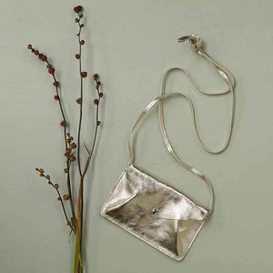 Goldfarbene, kleine Umhängetasche aus Leder neben einer Pflanze