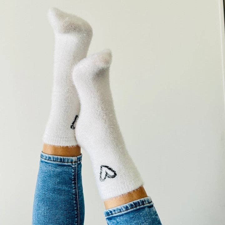 zwei Füße in weißen, kuscheligen Socjken mit schwarzem Herzumriss