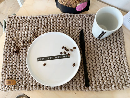 Aufsicht eingedecktes, handgestricktes Platzset in leinen mit weißem Teller und Tasse sowie schwarzem Messer