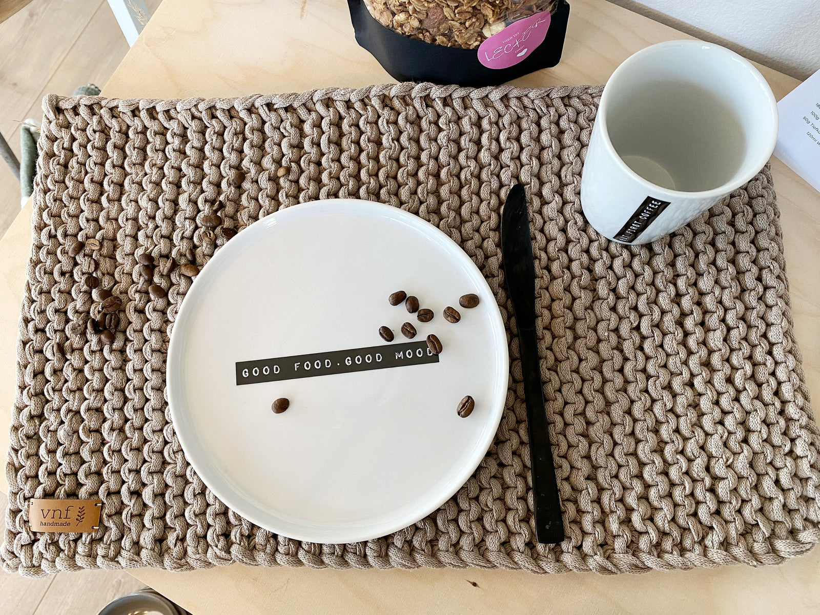 Aufsicht eingedecktes, handgestricktes Platzset in leinen mit weißem Teller und Tasse sowie schwarzem Messer