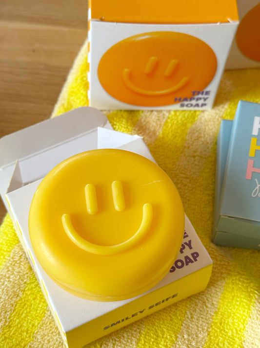 gelbe, runde seife mit Smiley auf dazugehöriger Verpackung, im Hintergrund die Seife in orange