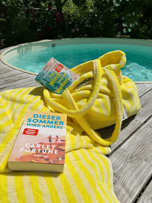 gelbe frotee accessoires und bücher auf dem holzboden vor einem runden pool
