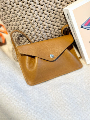 kleine, braune Umhängetasche aus Leder an ein Kissen gelehnt