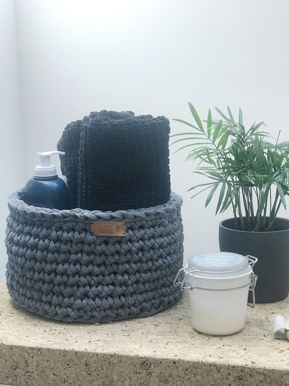 Hellgrauer Häkelkorb gefüllt mit Vorratsgläsern. Kücheninspiration mit Minzpflanze und einem Hlzbrett mit Gebäck