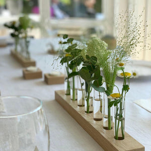 Tischdeko mit Blumenwiese von Stadtrandstil, gefüllt mit frischem Grün und Margariten, schemenhaft ist ein eingedeckter Tisch erkennbar