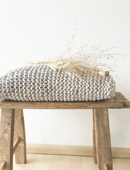 Hellgraues, handgestricktes Kissen aus Recyclingmix von Stadtrandstil. Natürlich dekoriert auf einer kleinen Holzbank aus Altholz und einem Bund getrockneter Gräser