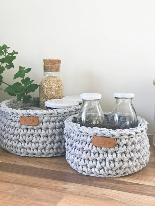 Zwei Häkelkörbe in hellem Grau gefüllt mit kleinen Flaschen und Kräutern. Als Beispiel für die DIY Häeklsets