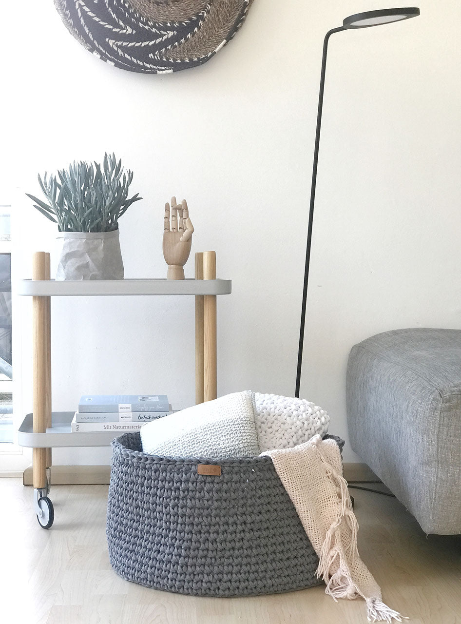 Wohnzimmer Inspiration im klaren Design: Moderner Beistellwagen mit Pflanze und Büchern dekoriert, eine schwarze Leselampe und dem extragroßem Häkelkorb von Stadtrandstil, in dem Kissen und eine Decke aufbewahrt werden