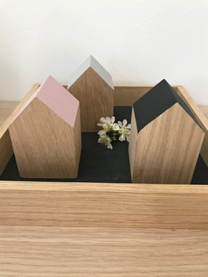 Drei kleine Dekohäuser aus Eichenholz, deren Giebel unterschiedlich lackiert sind. Je einmal in schwarz, rosé und sandstone. Sie stehen auf einem quadratischem Holztabeltt und sind mit einer zarten, kleinen Blume dekoiert