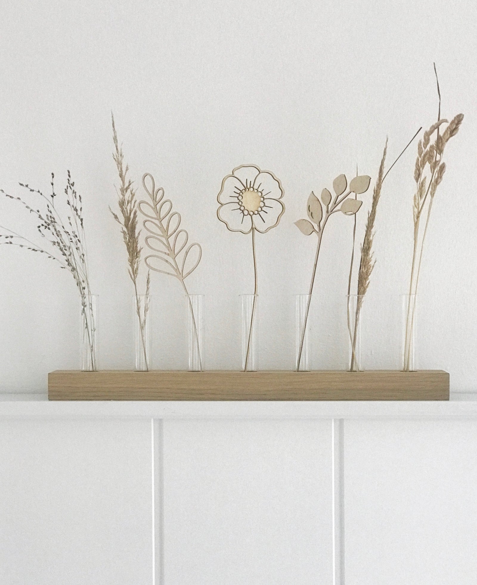 Schlichte Dekoration: minimalistisches Blumendisplay aus Holz, gefüllt mit Trockengräsern und Holzblumen vor weißem Hintergrung