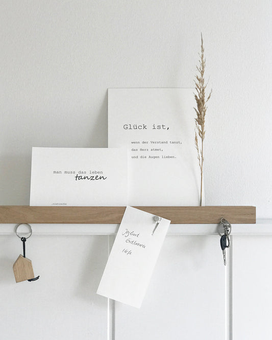 Wandleiste von Stadtrandstil handmade, natürlich und zeitlos dekoriert mit weißen Postkarten mit Text, einem getrocknetem Gras, einem Einkaufzettel. Fahrradschlüssel und einem Schlüsselanhänger in Hausform