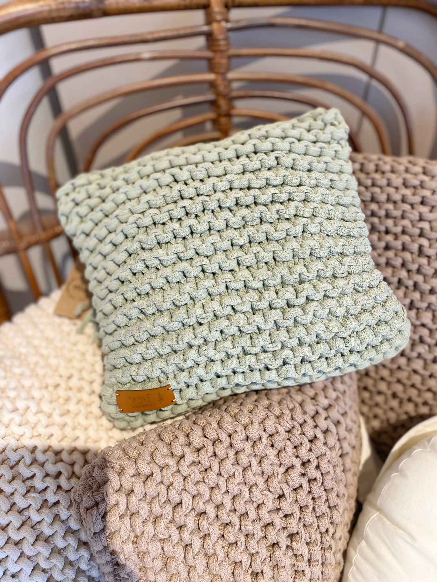 Mehrere kleine, handgearbeitete Kissen aus Recyclingmix in verschiedenen Naturtönen auf Rattansessel