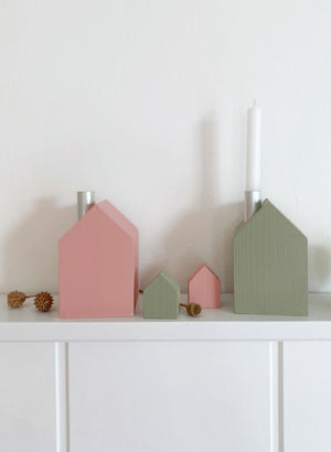 Auf einem weißen Bord stehen ein roséfarbenes Kerzenhaus, ein Minijhus in oliv und in rosé sowie en olivfarbenes Kerzenhaus in liv mi einer weißen Kerze. Schlichte Dekoration von Stadtrandstil