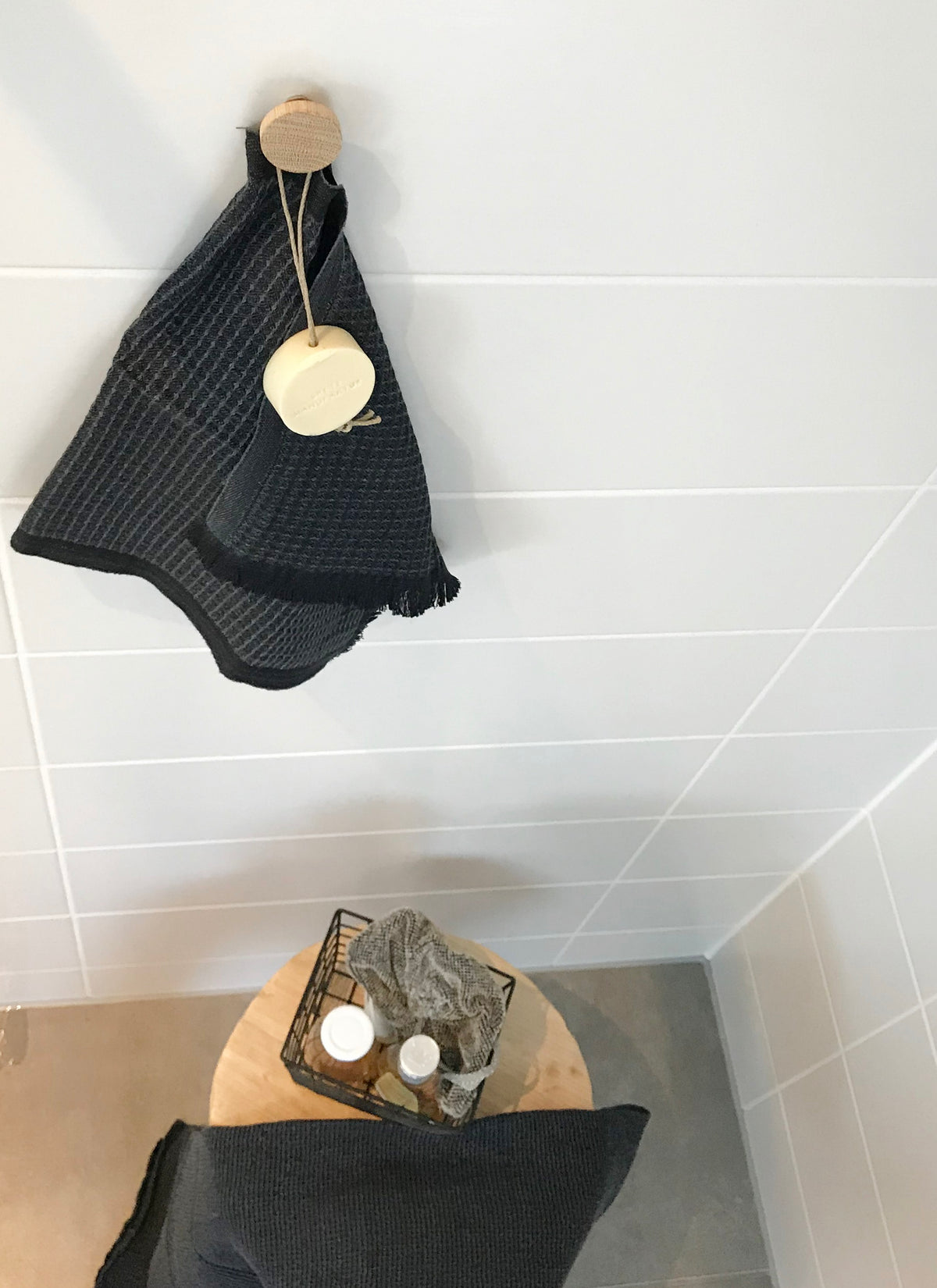 Badinspiration natürlich und zeitlos. Magnetpin aus Eiche, an dem ein kleines Handtuch und eine Seife hängen. Auf dem Boden stehet ein Holzhocker mit Badutensilien